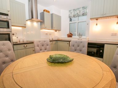 A kitchen with light green cabinets, a round wooden table with a green glass dish, and upholstered chairs at Pottergill in Windermere