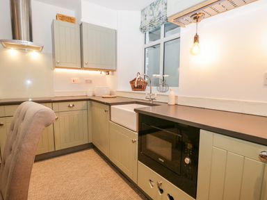 A kitchen with green cabinets a black microwave a white sink and a window above the sink at Pottergill in Windermere
