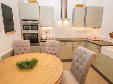 A kitchen with green cabinets a round wooden table and grey cushioned chairs at Pottergill in Windermere