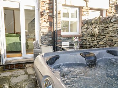 A stone patio with a hot tub a table with flowers and glasses and chairs at Pottergill in Windermere