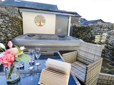 An outdoor patio area with a hot tub glass table chairs a vase of flowers and a book at Pottergill in Windermere