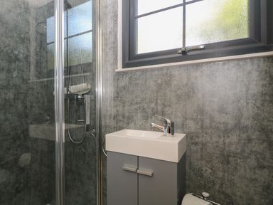 A bathroom with a glass shower enclosure a small sink with a cabinet and a window at High Rigg Shepherd's Hideaway in Brampton Cumbria