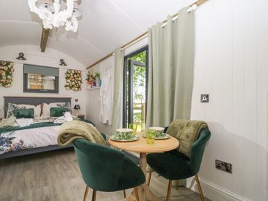 A small bedroom with a bed floral bedding a round wooden table with two green chairs and cups at High Rigg Shepherd's Hideaway in Brampton Cumbria
