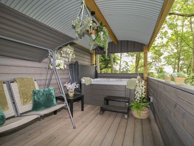 A covered wooden deck with a swing seat a hot tub and potted plants at High Rigg Shepherd's Hideaway in Brampton Cumbria