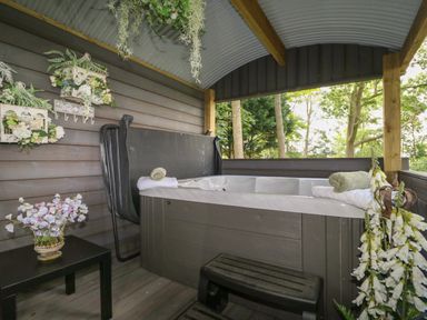 A covered outdoor hot tub with towels flowers and wall decorations at High Rigg Shepherd's Hideaway in Brampton Cumbria