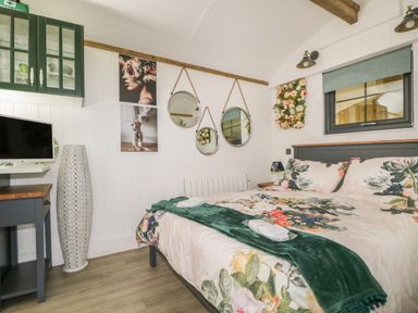 A bedroom with a bed floral bedding pillows and blanket three round mirrors hanging on the wall near window at High Rigg Shepherd's Hideaway in Brampton Cumbria