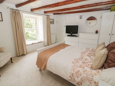 A bedroom with a bed a window with curtains a dresser with a television and a mirror on the wall at 1A Chantry Place in Morpeth