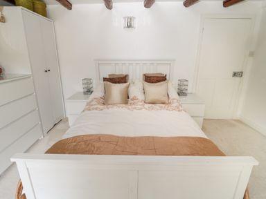 A bedroom with a white bed frame and beige bedding with pillows bedside tables on each side and white wardrobe and drawers at 1A Chantry Place Morpeth