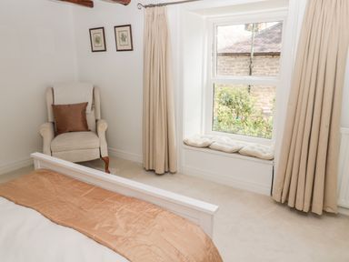 A bedroom with a bed a beige armchair and a window seat with cushions at 1A Chantry Place in Morpeth