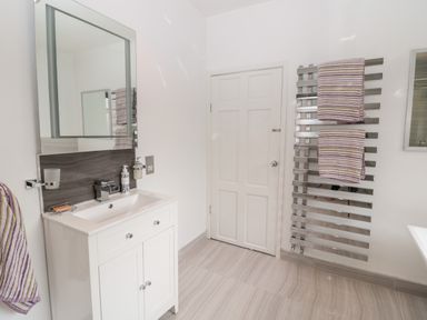 A bathroom with a white vanity sink and mirror a door and a wall-mounted towel radiator with striped towels at 1A Chantry Place in Morpeth