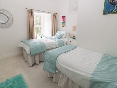 A bedroom with two single beds and a window with beige curtains at 1A Chantry Place in Morpeth