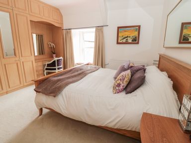 A bedroom with a wooden bed and wardrobe and a chair by a window at 1A Chantry Place in Morpeth