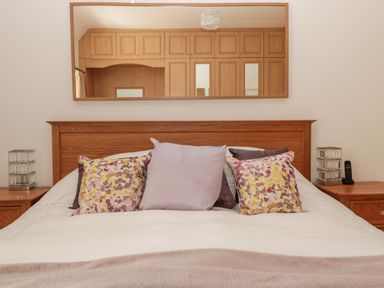 A bedroom with a wooden headboard a bed with five decorative pillows a blanket on the bed two bedside tables with lamps a mirror reflecting wooden cabinets at 1A Chantry Place in Morpeth