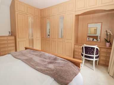 A bedroom with wooden wardrobes a dressing table with a mirror and chair and a bed with a blanket at 1A Chantry Place in Morpeth