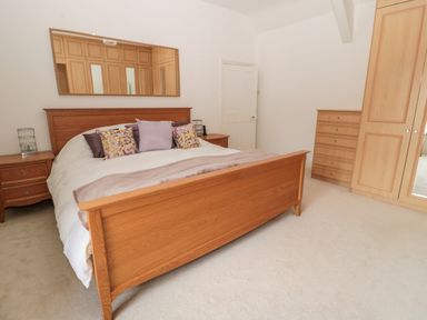 A bedroom with a wooden bed a mirror on the wall and wooden wardrobes at 1A Chantry Place in Morpeth