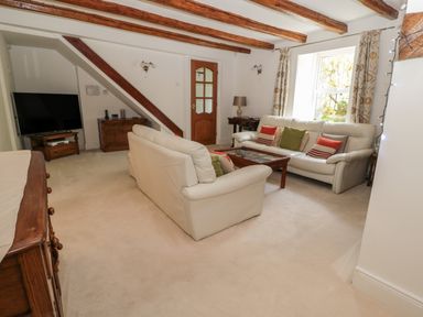 A living room with two white sofas a wooden coffee table a television a wooden sideboard and exposed wooden ceiling beams at 1A Chantry Place in Morpeth