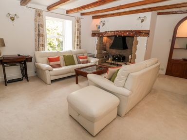 A living room with white sofas a wooden coffee table a stone fireplace and exposed wooden ceiling beams at 1A Chantry Place in Morpeth