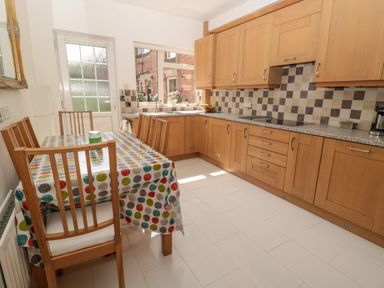 A kitchen with wooden cabinets a dining table with chairs and a door leading outside at 1A Chantry Place in Morpeth
