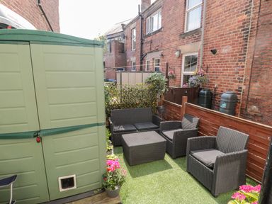 An outdoor patio area with black wicker furniture and a green storage shed at 1A Chantry Place in Morpeth