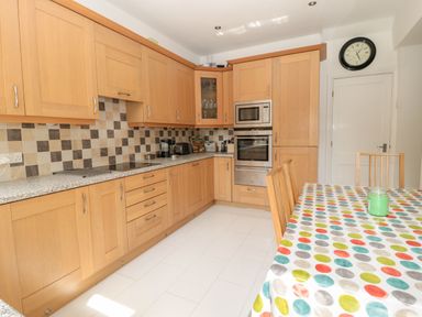 A kitchen with wooden cabinets checkerboard tile backsplash and a dining table with multicolored polka dot tablecloth at 1A Chantry Place in Morpeth