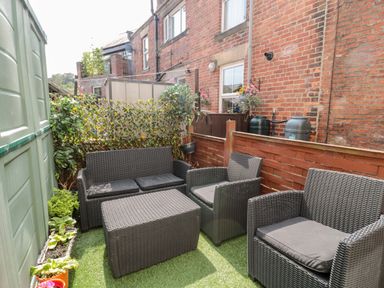 An outdoor seating area with black wicker furniture and artificial grass at 1A Chantry Place in Morpeth