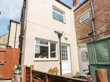 An outdoor backyard area with a white door and window on a beige building next to a brick wall and a wooden fence at 1A Chantry Place Morpeth