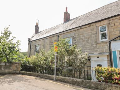 A stone house with two chimneys and a small front garden behind a black metal fence at 1A Chantry Place in Morpeth