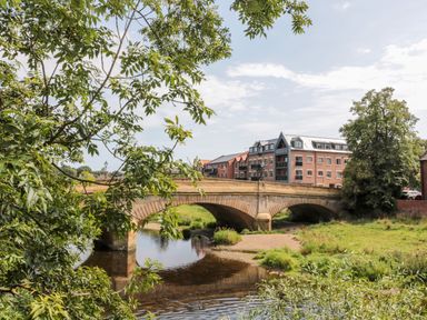 A stone bridge over a river with apartment buildings and trees at 1A Chantry Place in Morpeth