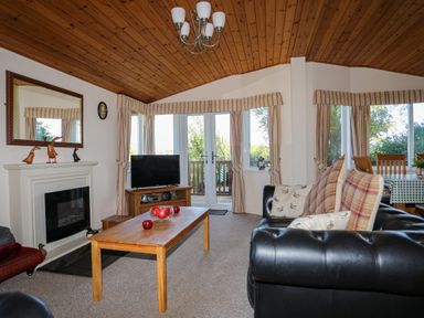 A living room with a wooden coffee table black sofa and a fireplace at Ffrwd Lodge in Rhosneigr