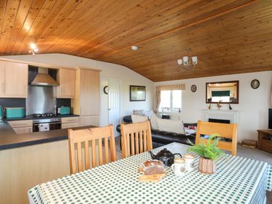 A dining table with chairs and a tea set in an open plan kitchen and living room at Ffrwd Lodge in Rhosneigr