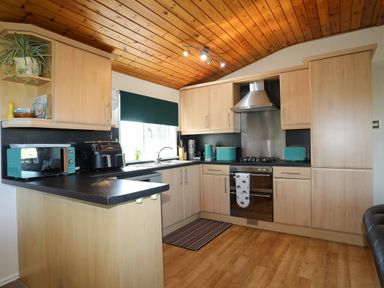 A kitchen with wooden cabinets black countertops and a stainless steel oven at Ffrwd Lodge in Rhosneigr