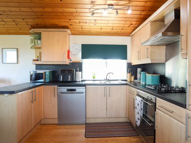 A kitchen with wooden cabinets a gas stove an oven a dishwasher a toaster an air fryer a sink and a window at Ffrwd Lodge in Rhosneigr