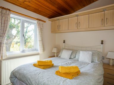 A bedroom with a bed with folded yellow towels and pillows under wooden cabinets at Ffrwd Lodge in Rhosneigr