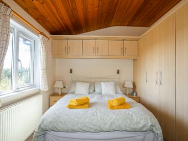 A bedroom with a double bed yellow towels bedside tables lamps overhead cupboards and a window at Ffrwd Lodge in Rhosneigr