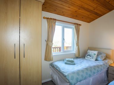 A bedroom with a wooden wardrobe a bed with polka dot bedding and folded towels on top by a window with curtains at Ffrwd Lodge in Rhosneigr
