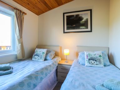 A bedroom with two single beds bedside table lamp and window at Ffrwd Lodge in Rhosneigr