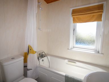 A bathroom with a toilet a bathtub a shower curtain and a window at Ffrwd Lodge in Rhosneigr