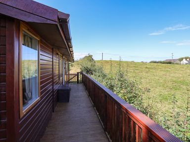 A wooden balcony with railing overlooking a grassy field at Ffrwd Lodge in Rhosneigr