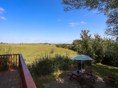 A garden with a picnic table and umbrella next to a wooden deck overlooking a green field at Ffrwd Lodge in Rhosneigr