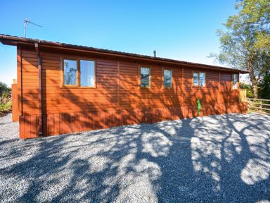 A wooden cabin with multiple windows and gravel ground at Ffrwd Lodge in Rhosneigr