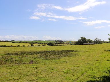 A grassy field with trees and a building in the distance under a partly cloudy sky at Ffrwd Lodge in Rhosneigr