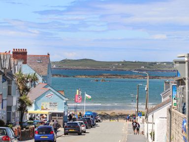 A street with parked cars and people walking leading to a beach with a surf shop and ocean in the background at Ffrwd Lodge in Rhosneigr