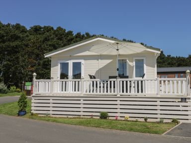 A white cabin with a deck and umbrella in front of trees at Jonstone Pines in Cayton Bay near Scarborough