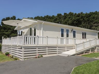 A white mobile home with a raised deck and ramp with a white umbrella surrounded by trees at Jonstone Pines in Cayton Bay near Scarborough