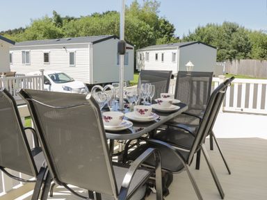 An outdoor patio with a glass table and six chairs set with dishes and glasses at Jonstone Pines in Cayton Bay near Scarborough