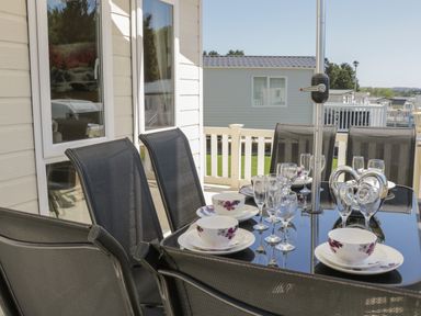 An outdoor dining table set with plates cups and glasses surrounded by black chairs on a patio at Jonstone Pines in Cayton Bay near Scarborough