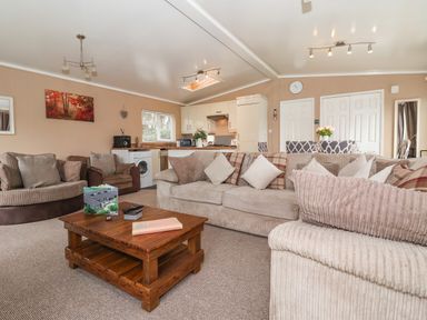 A living room with beige sofas and a wooden coffee table with a kitchen and dining area in the background at Jonstone Pines in Cayton Bay near Scarborough