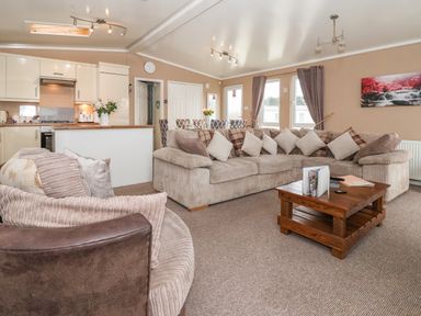 A living room with sofas cushions and a wooden coffee table next to an open kitchen and dining area at Jonstone Pines in Cayton Bay near Scarborough