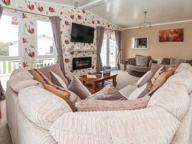 A living room with a large sectional sofa and coffee table a wall-mounted TV and fireplace with floral wallpaper at Jonstone Pines in Cayton Bay near Scarborough