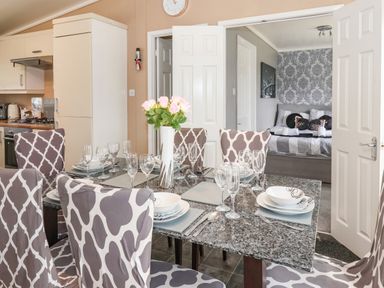 A dining area with a granite table set with plates glasses and a vase of flowers and a view into a bedroom at Jonstone Pines in Cayton Bay near Scarborough